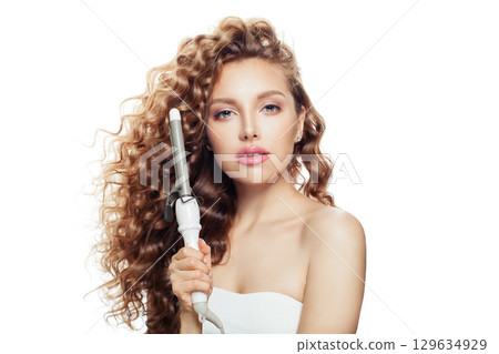 Glorious young model woman with long curly wavy hairstyle showing hot curling tongs iron  129634929