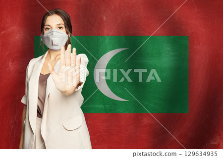 Confident woman in medical mask showing stop gesture open palm hand against flag 129634935