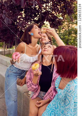 Young people playfully feeding each other donuts on park bench Young people playfully feeding each other donuts on park bench 129635134