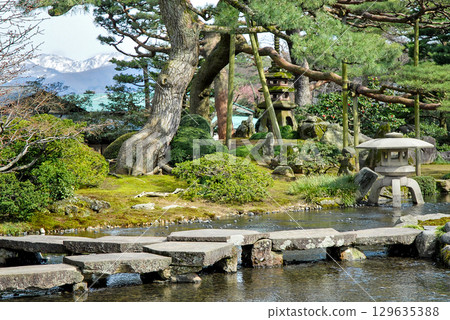 Kenrokuen Garden's Gankobashi Bridge and snow-capped mountains, a charming early spring scene in a Japanese garden Kenrokuen Garden's Gankobashi Bridge and snow-capped mountains, a charming early spring scene in a Japanese garden 129635388