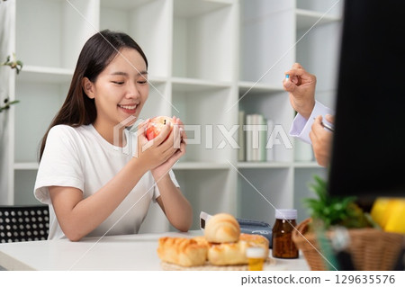 Dietary Consultation. Young woman receiving nutrition advice from a doctor with fruits and baked goods. 129635576