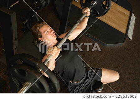 Young caucasian man or bodybuilder exercising bench press at fitness center. Young caucasian man or bodybuilder exercising bench press at fitness center. 129635602