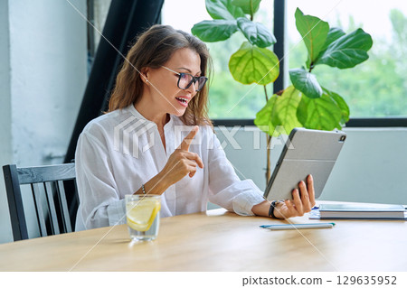 Middle aged female teacher entrepreneur using digital tablet for video online meeting 129635952