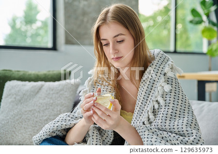Young woman under blanket with cup with lemon, at home on sofa 129635973