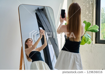 Smiling young teenage female taking selfie photo on smartphone 129636016