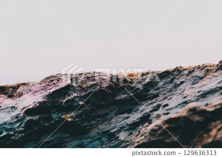 Colorful texture of rock formations against a pale sky at a coastal location 129636313