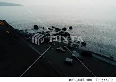 Dark rocky shoreline with calm waters during early morning fog 129636728