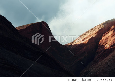 Mountains in dramatic light with clouds looming overhead at sunset 129636735