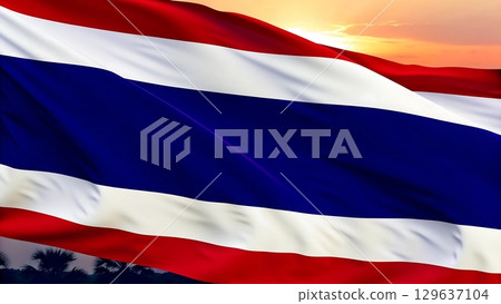 A waving thailand flag against a sunset sky with silhouetted trees below 129637104