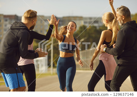 Happy young people giving high five to a woman rejoicing the success in sport training outdoors. 129637146