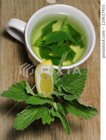 Fresh melissa leaves, lemon and ginger near a cup of melissa tea on a wooden surface vertical stock photo photo 129637455
