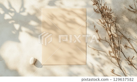 Blank kraft paper card mockup styled with soft botanical shadows and natural elements on textured concrete wall in minimal neutral tones with backlit morning light 129637582