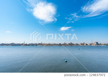 Serene Nile River View From Esna Lock Showing Luxor Cityscape Under Blue Sky. Serene Nile River View From Esna Lock Showing Luxor Cityscape Under Blue Sky. 129637972