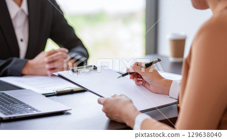 A scene of a businesswoman taking notes at a business meeting, listening to what is being said 129638040