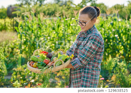 Portrait of woman showing basket with different fresh vegetables and herbs in garden 129638525
