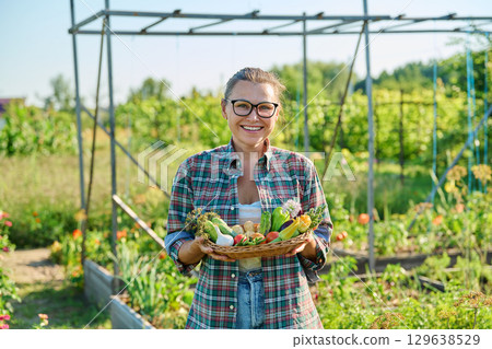 Portrait of woman showing basket with different fresh vegetables and herbs in garden 129638529