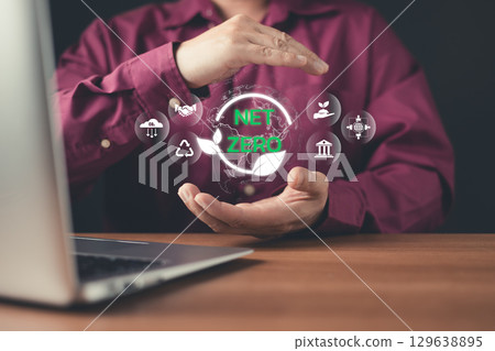 A man presents a glowing "Net Zero" digital hologram with sustainability icons, symbolizing carbon neutrality, renewable energy, and environmental responsibility in business and technology. 129638895