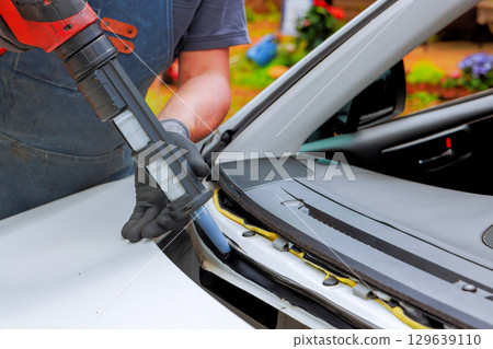 Vehicle repair process at an outdoor workshop with mechanic using power tools on car dashboard 129639110