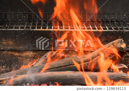 Flames dance as wood ignites in barbecue grill during summer gathering in backyard setting Flames dance as wood ignites in barbecue grill during summer gathering in backyard setting 129639113