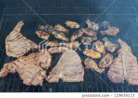 Delicious meats grilling over charcoal in backyard setting during sunny afternoon Delicious meats grilling over charcoal in backyard setting during sunny afternoon 129639115