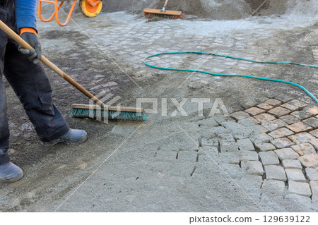 Worker sweeping cobblestone street with tools in construction site during work day hours 129639122