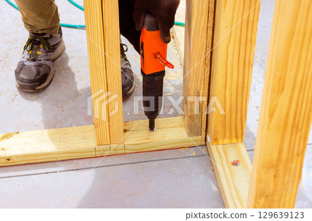 Construction worker using power air gun tool to assemble wooden framing structure 129639123