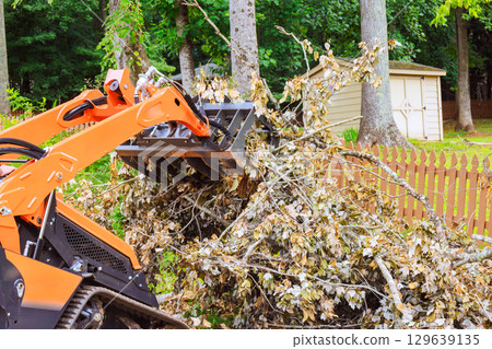 Heavy machinery clears fallen branches in residential yard after tornado Heavy machinery clears fallen branches in residential yard after tornado 129639135