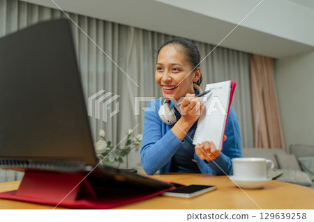 A Focused Woman Engaging in an Online Meeting Using Her Laptop and Notepad A Focused Woman Engaging in an Online Meeting Using Her Laptop and Notepad 129639258