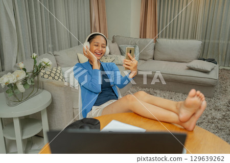 A Cheerful Young Woman Is Enjoying a Video Call at Home While Wearing Headphones A Cheerful Young Woman Is Enjoying a Video Call at Home While Wearing Headphones 129639262
