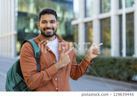 Young man with a backpack, smiling and pointing confidently, captured in an urban environment. Young man with a backpack, smiling and pointing confidently, captured in an urban environment. 129639448