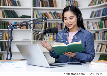 A woman sits in a library, using headphones and a studio microphone while recording her podcast. 129639453