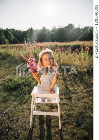 Little girl holding flowers in ice cream cone in a sunlit field with blooming plants during golden Little girl holding flowers in ice cream cone in a sunlit field with blooming plants during golden 129640003