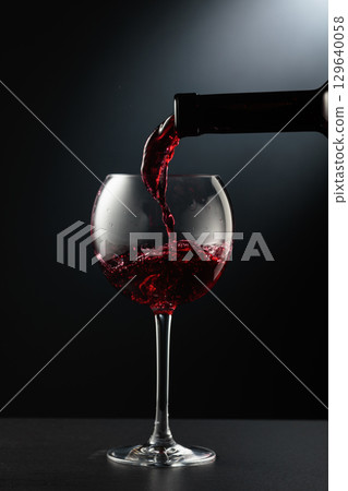 Pouring red wine into a wine glass. 129640058