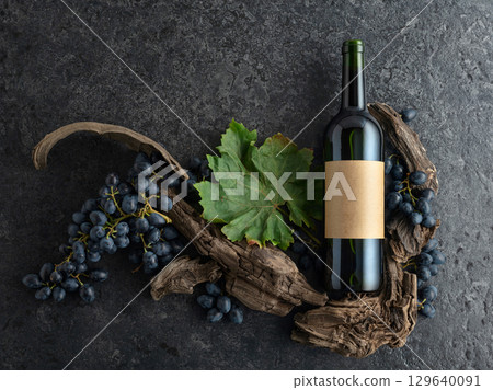 Bottle of red wine, blue grapes, and old vine snags on a black stone background. 129640091