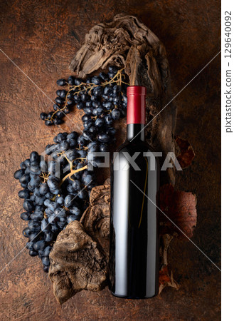Bottle of red wine with blue grapes and old weathered snags. 129640092