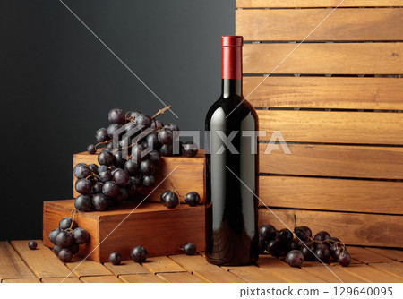 Bottle of red wine and blue grapes on a wooden background. 129640095