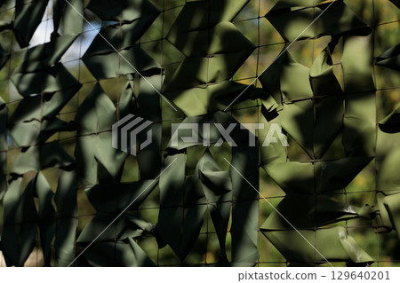 Intricate Patterns of Green Fabric Mesh Creating a Unique Camouflage Effect in Nature's Lush Background, Offering a Blend of Texture and Depth in Outdoor Settings 129640201