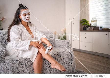 Young Woman Removing Leg Hair While Wearing a Face Mask at Home 129640262