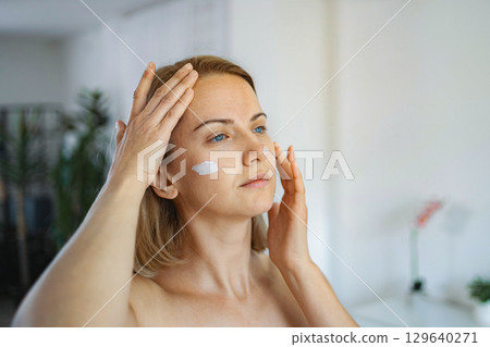 Woman applying face cream at home for her daily skincare routine Woman applying face cream at home for her daily skincare routine 129640271