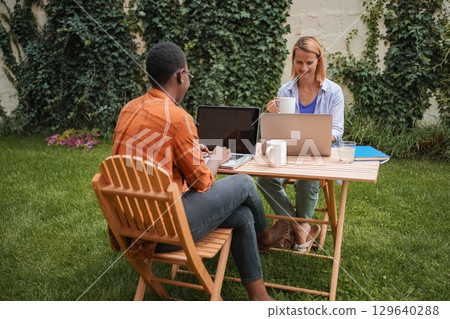 Two young professionals working remotely on laptops in a garden 129640288