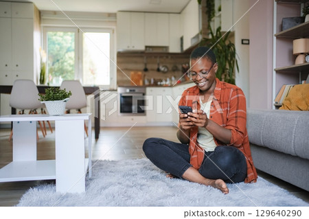 Young Woman Using Smartphone at Home, Relaxing on the Floor Young Woman Using Smartphone at Home, Relaxing on the Floor 129640290