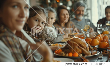 A diverse group of people enjoying a Thanksgiving Day meal. The table is set with a turkey and festive decorations 129640359
