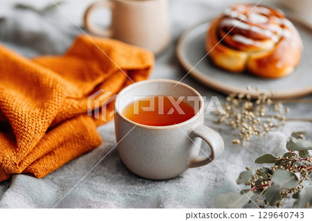 Warm tea on a cozy dining table with a sweet cinnamon roll and a soft blanket Warm tea on a cozy dining table with a sweet cinnamon roll and a soft blanket 129640743