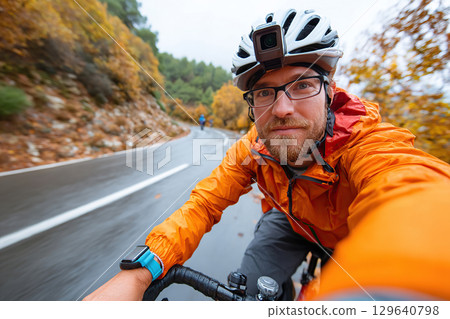 Cyclist enjoying a rainy ride through autumn foliage on a winding road 129640798