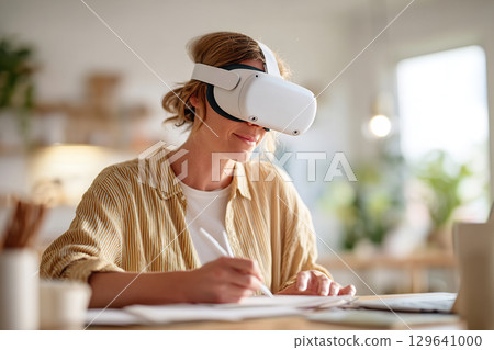 Woman taking notes while engaged in a virtual reality learning experience at home Woman taking notes while engaged in a virtual reality learning experience at home 129641000