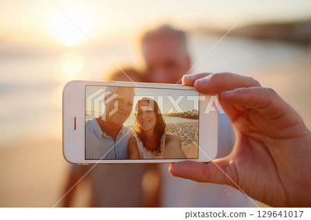 Couple enjoying a sunset selfie with AR filter effects on the beach in warm light 129641017