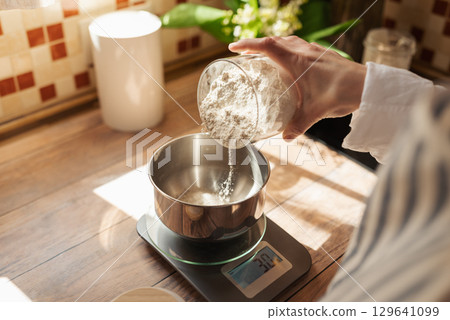 Woman making dough for a bread. Close up of hands of a girl adding some flour to dough, following recipe of baking bread Woman making dough for a bread. Close up of hands of a girl adding some flour to dough, following recipe of baking bread 129641099