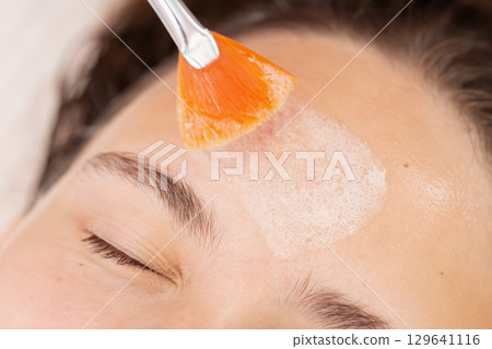 Cleaning of the face of young female client at beauty clinic before the next procedures, close up. Concept of doing professional skincare treatment, health care and therapy 129641116