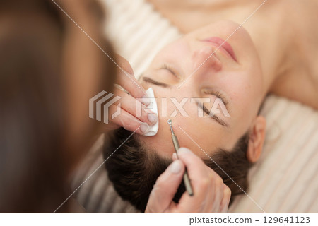 Professional cosmetology procedure for cleansing pores and skin from defects in a beauty salon. Close up shot of using facial metal device for the mechanical cleaning of skin 129641123