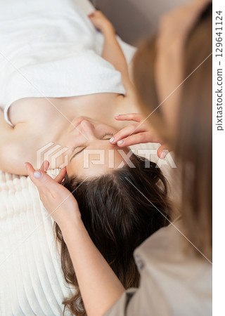 Vertical shot of cosmetologist making face massage, close up. Young woman getting massage treatment at beauty spa salon, concept of skin and body care, facial beauty treatment 129641124